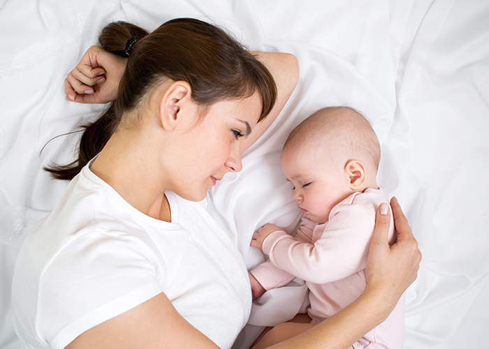 お母さんが横たわって、赤ちゃんを抱き寄せながら見つめている写真｜不妊治療HP