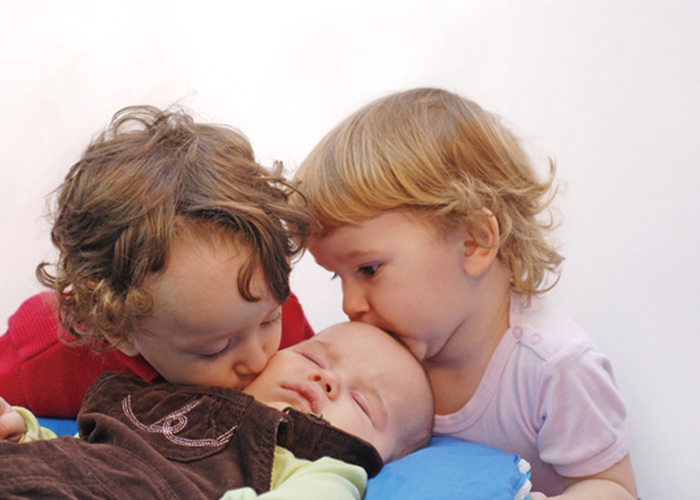 二人の子どもが赤ちゃんにキスしている写真｜不妊治療HP