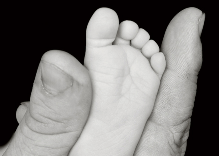 大人の手で赤ちゃんの足の裏をつまんでいるモノクロ写真｜不妊治療HP